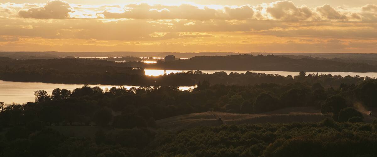 A sunset over a lake with surrounding hills and trees.