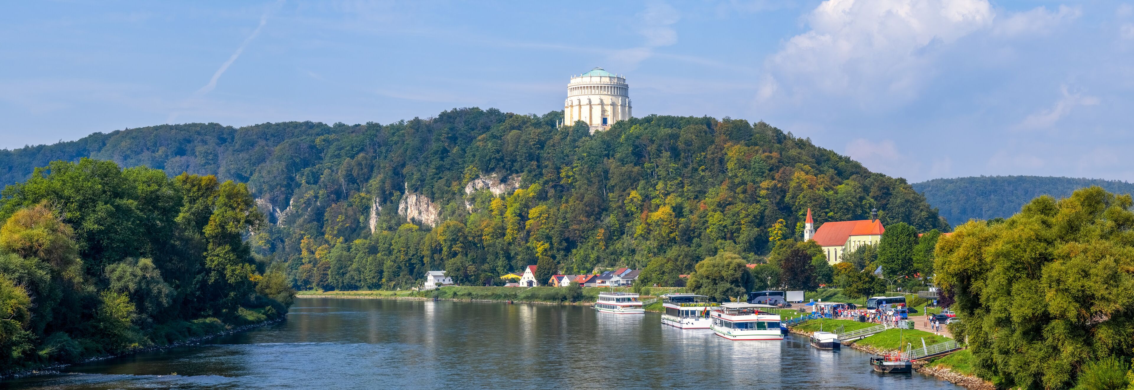 A river with boats, a water tower, and a church on a hill.