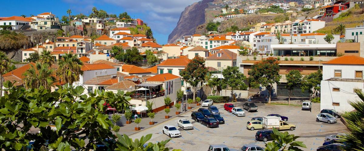 A coastal town with terraced houses, a parking lot, and a mountain in the background.
