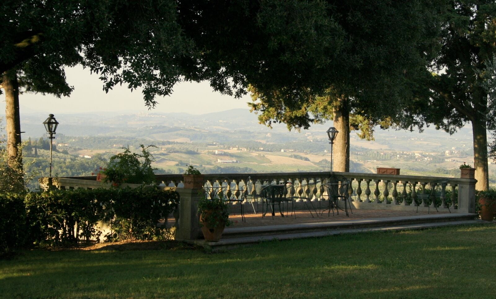 Un jardín con vistas a colinas distantes y una zona pavimentada con sillas y mesas.