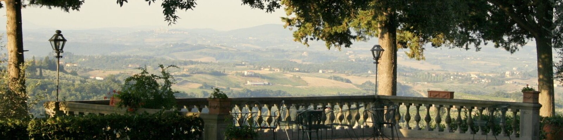Un jardín con vistas a colinas distantes y una zona pavimentada con sillas y mesas.