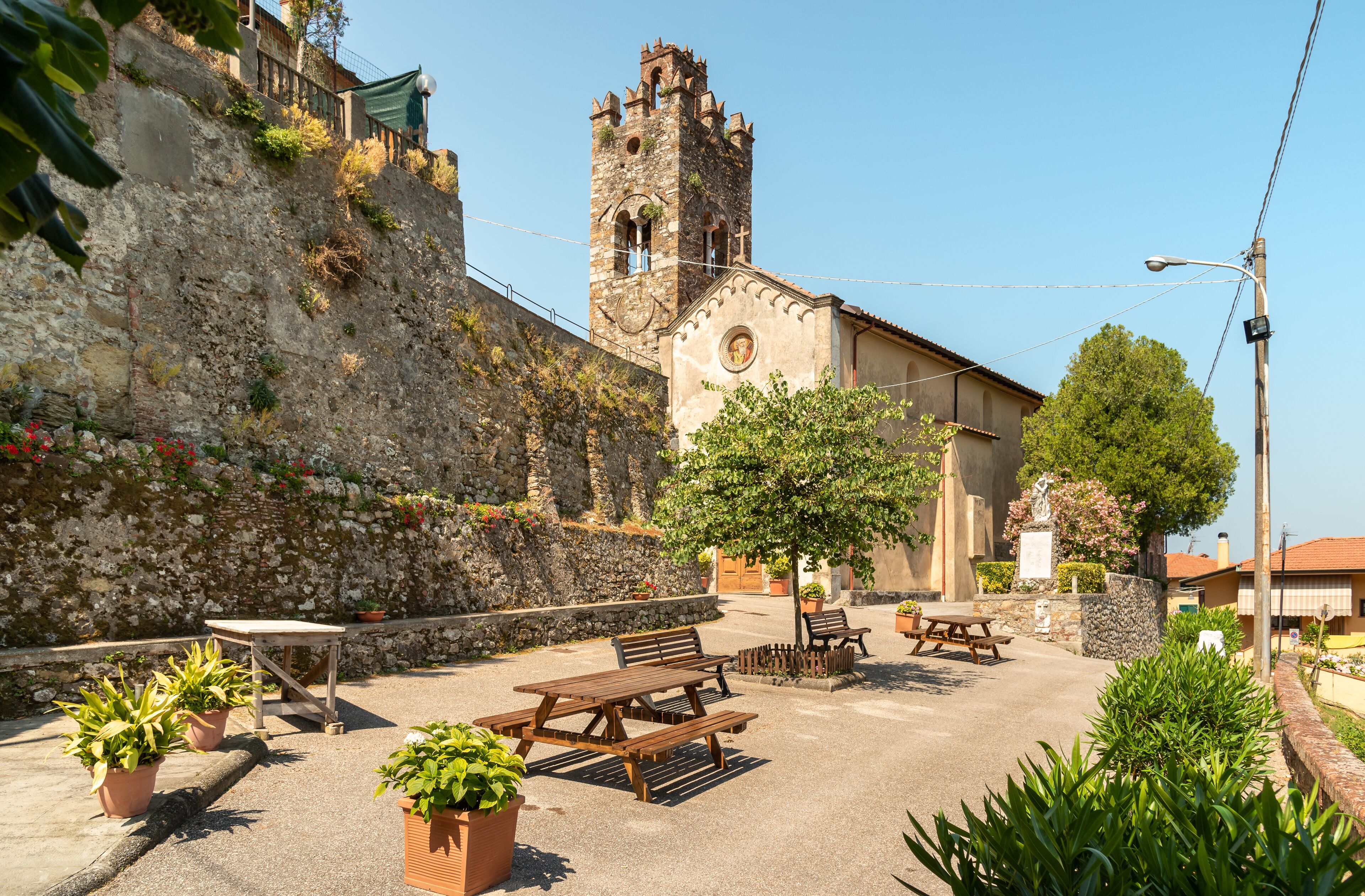 A stone wall, a wooden bench, a picnic table, a church with a bell tower, and potted plants.