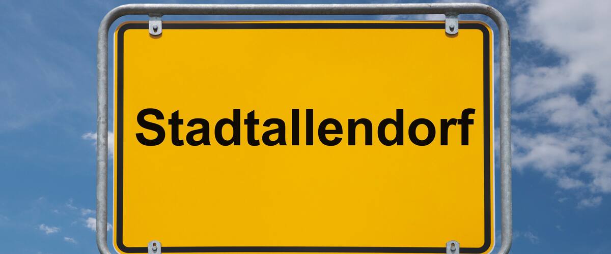 A yellow sign with the text "Stadtallendorf" against a blue sky with clouds.