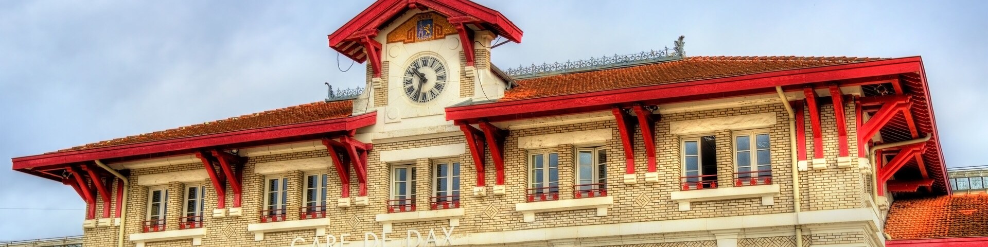 Un edificio con torre de reloj, techo rojo y ventanas arqueadas.