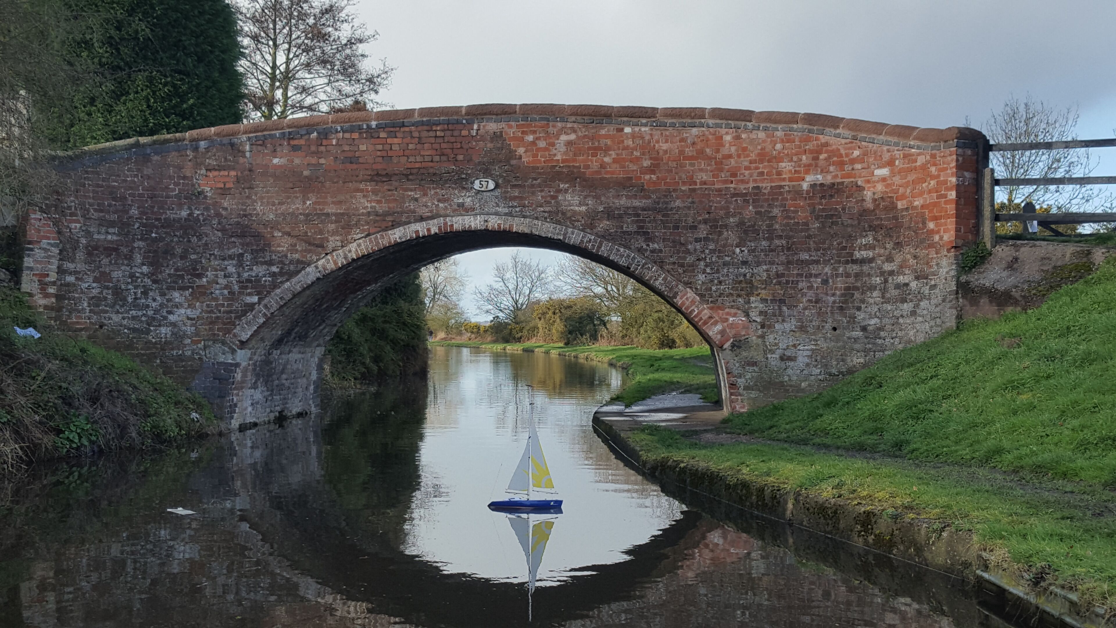 A brick bridge over a canal with a sailboat.