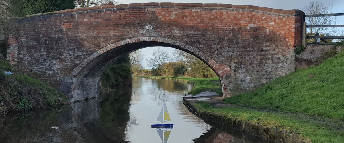 A brick bridge over a canal with a sailboat.