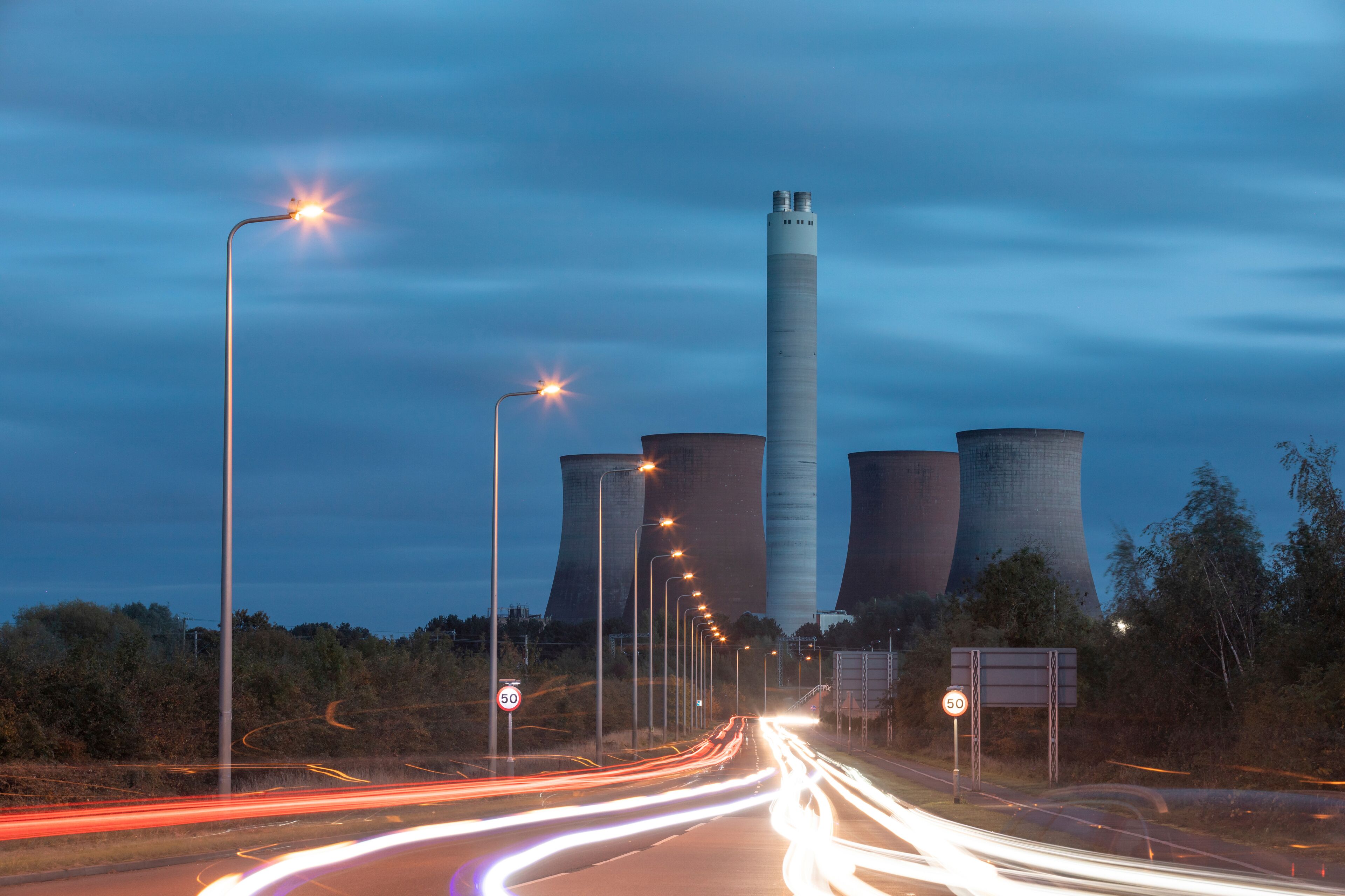 A highway with light trails, a tall cooling tower, and a sign indicating a speed limit of 50.