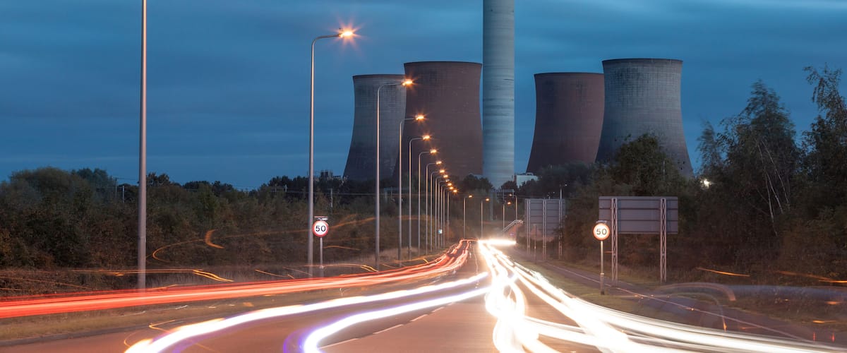 A highway with light trails, a tall cooling tower, and a sign indicating a speed limit of 50.