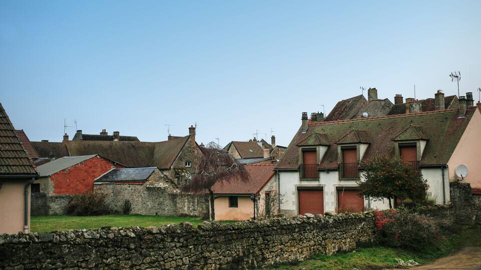 A rural village with stone walls, traditional houses with red roofs, and a clear blue sky.