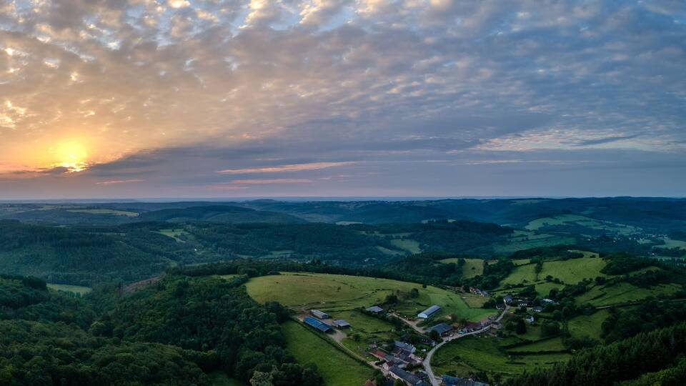 A valley with rolling hills, scattered houses, and a sunset.