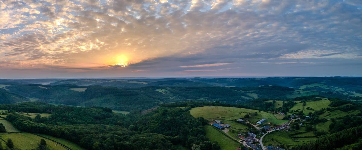 A valley with rolling hills, scattered houses, and a sunset.