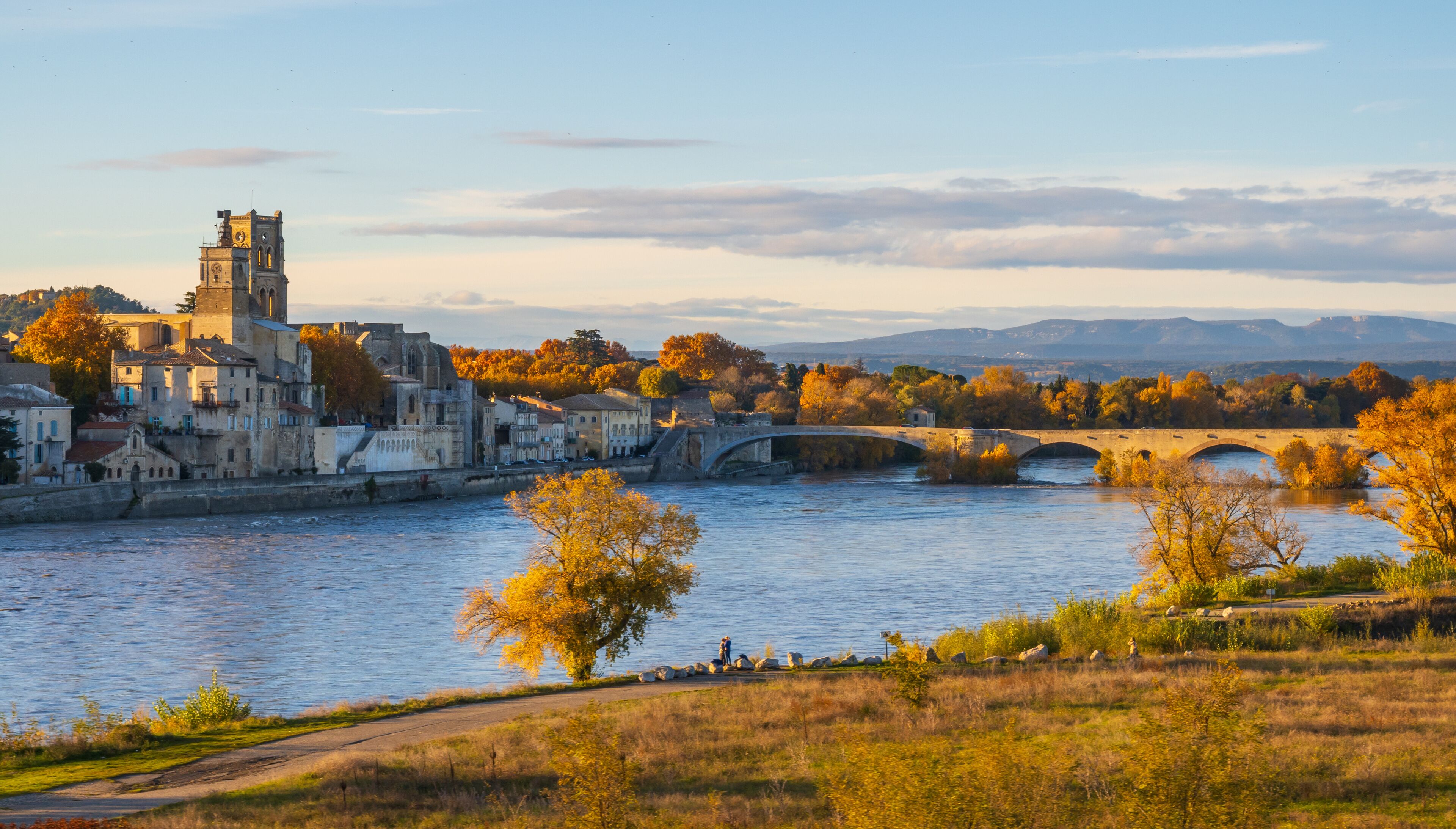 A river with a stone bridge, historic buildings, and autumn trees.
