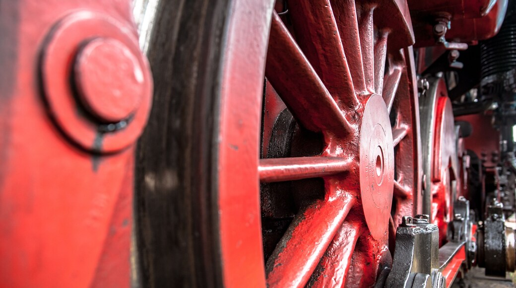 Red spoke wheels with rods and pistons of old train locomotive at ubex location with authentic industrial details and craftsmanship along the rail way and station