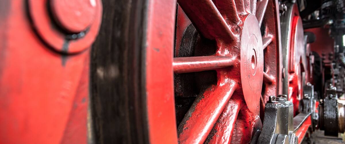 A close-up of a red metal wheel with bolts and a circular component.