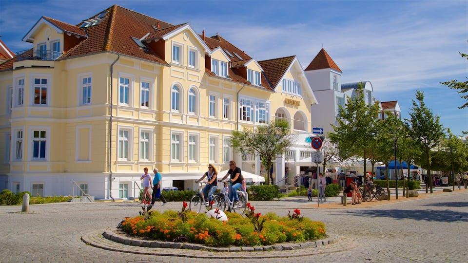 A cobblestone square with a yellow building, people on bicycles, and a flower garden.