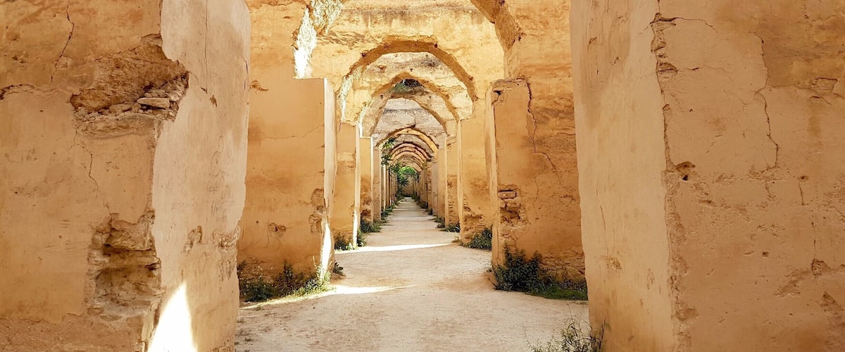 A long, arched corridor with weathered walls and a dirt path.