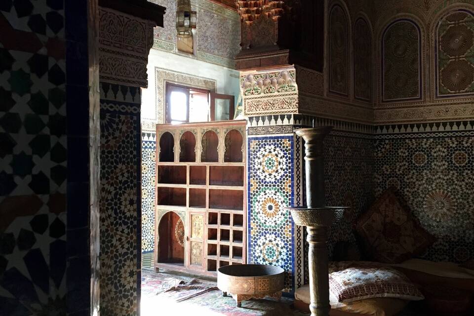 An interior with intricate tile work, a wooden door, and a traditional lamp.