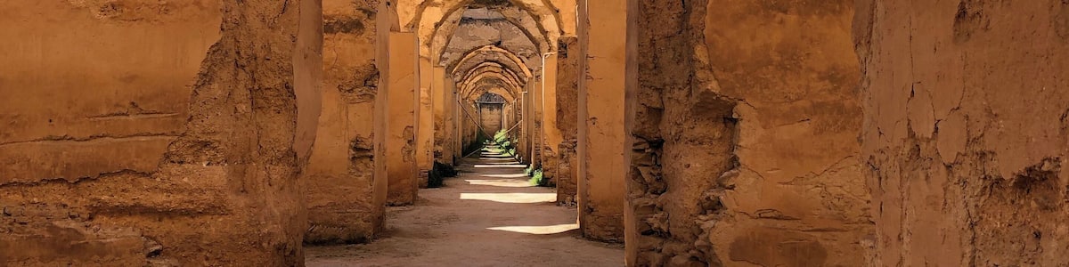 A long corridor with arches and a dirt floor.