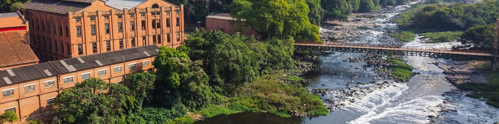 Un río serpentea por un paisaje exuberante con un puente, un edificio de ladrillo y abundante vegetación.