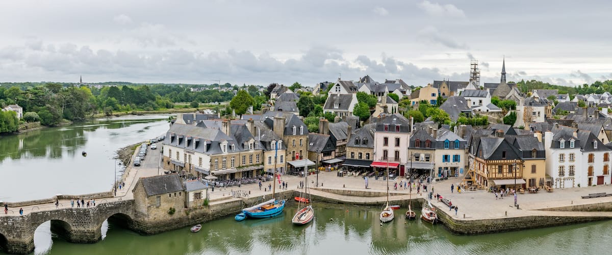 A riverside town with historic buildings, a bridge, and boats docked along the water.