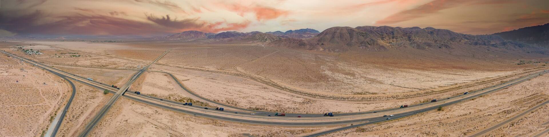 a stunning aerial panoramic shot of majestic mountain ranges in a vast desert land with powerful clouds with freeways filled with cars in Yermo California USA