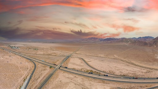 a stunning aerial panoramic shot of majestic mountain ranges in a vast desert land with powerful clouds with freeways filled with cars in Yermo California USA