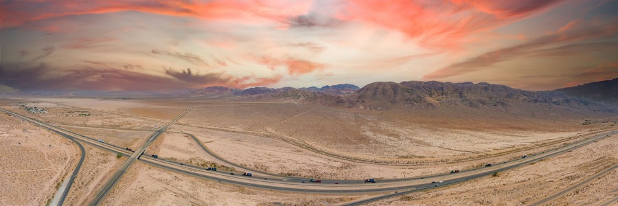 A desert landscape with a highway and mountains in the background.