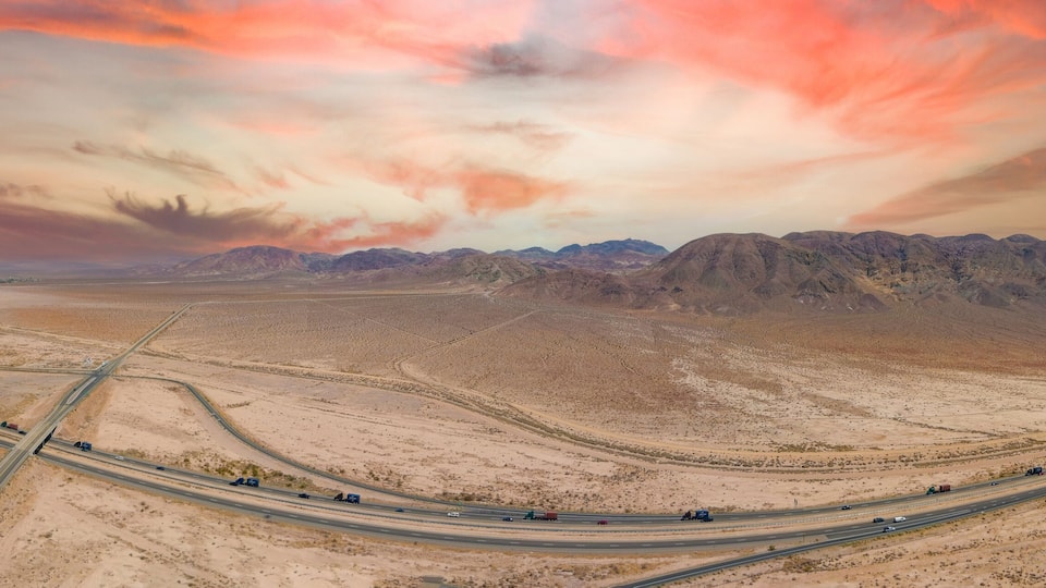 A desert landscape with a highway and mountains in the background.