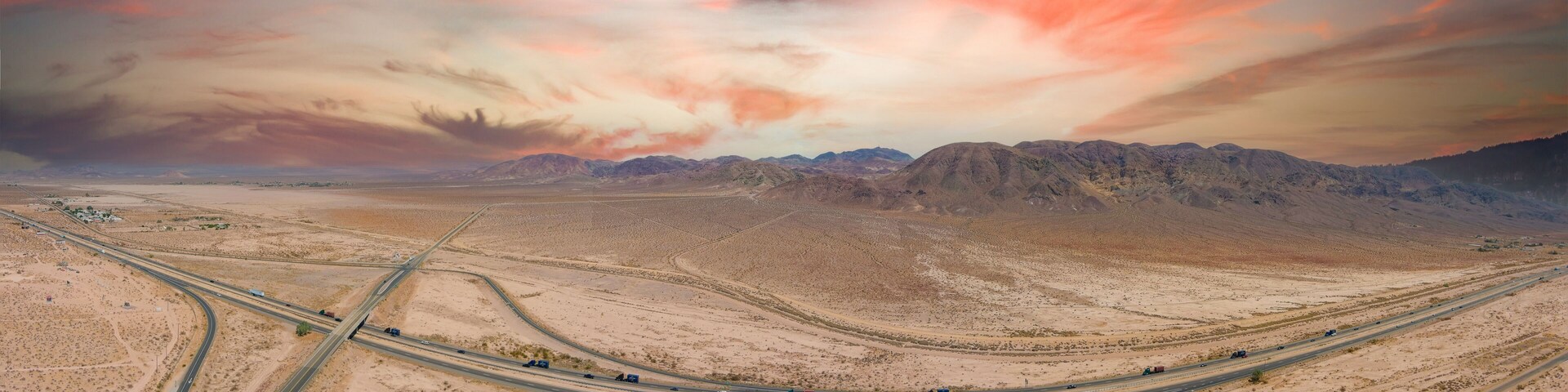 a stunning aerial panoramic shot of majestic mountain ranges in a vast desert land with powerful clouds with freeways filled with cars in Yermo California USA