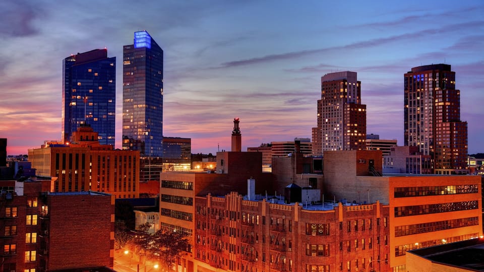 A city skyline at dusk with illuminated buildings and a clear sky.