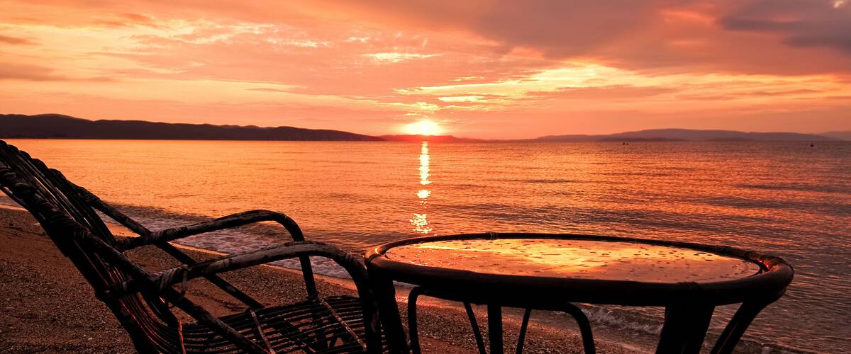A beach chair and table facing a sunset over water.