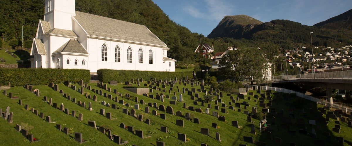 A church with a steeple, a cemetery, and a bridge in the background.