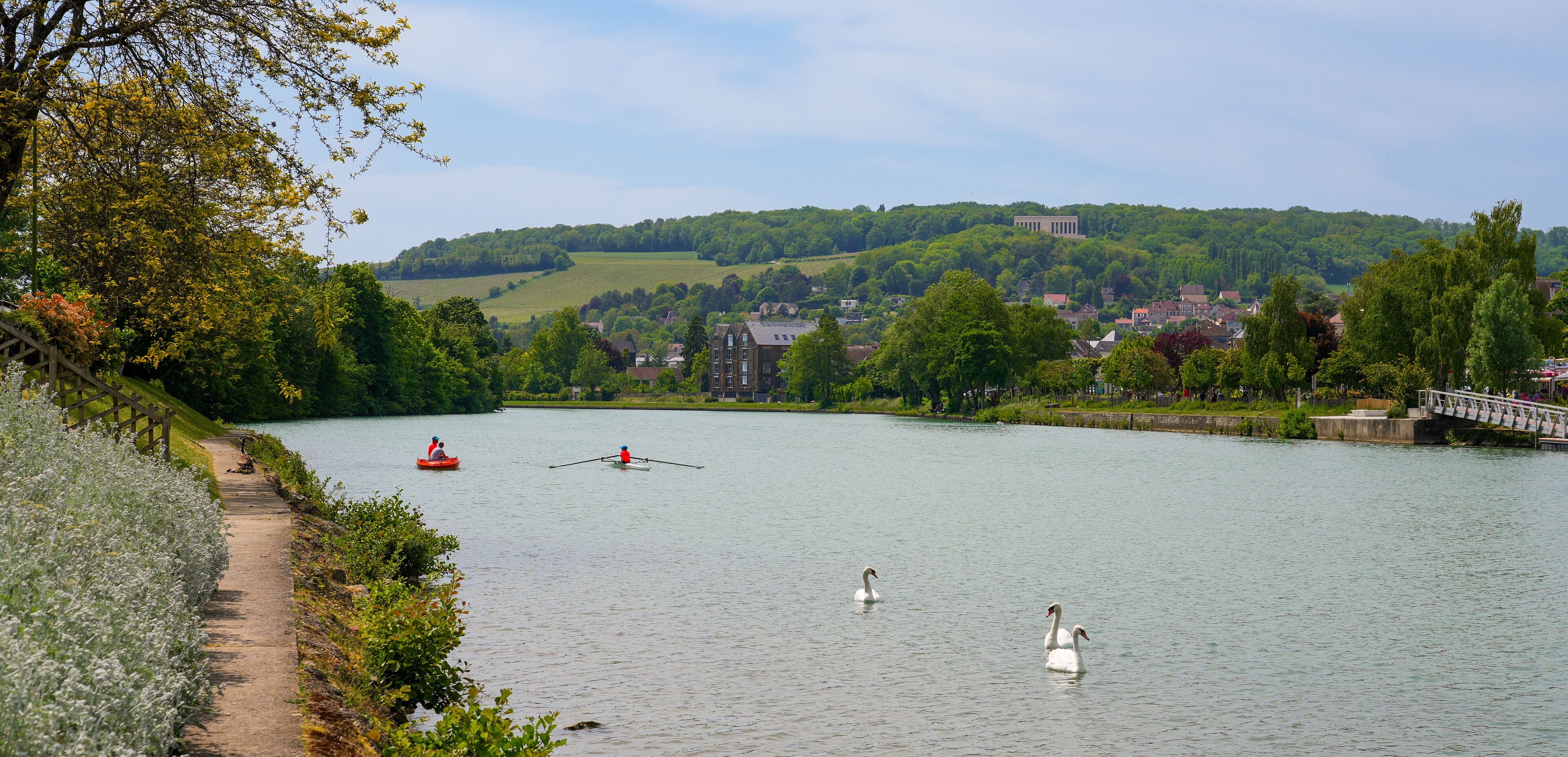 A calm river with swans, a rowboat, and a bridge.
