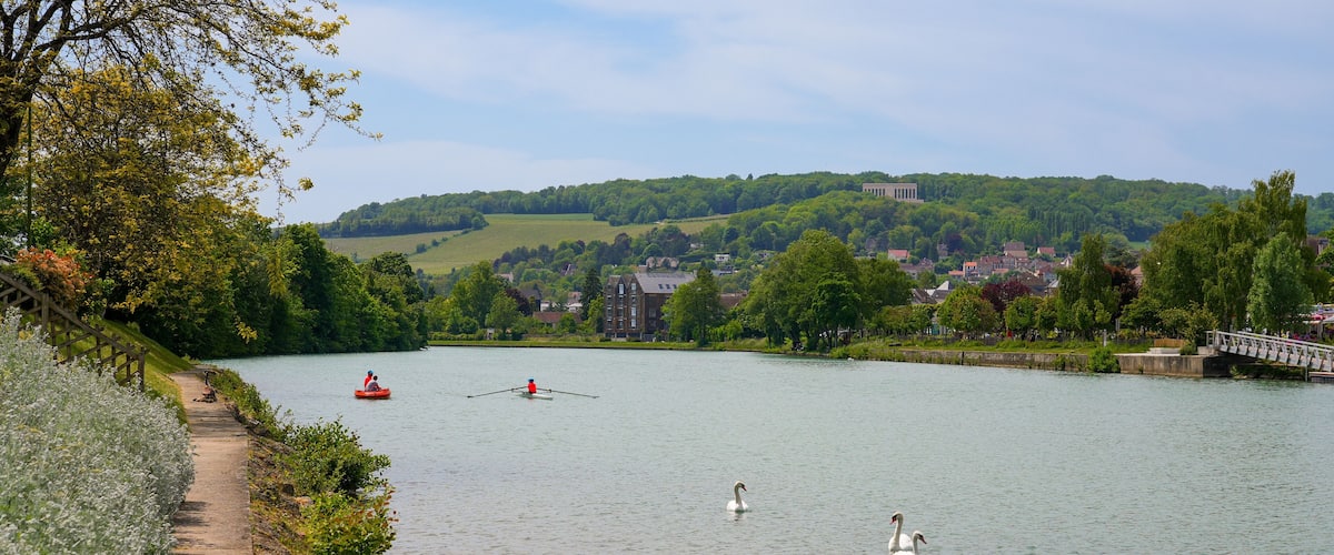 A calm river with swans, a rowboat, and a bridge.