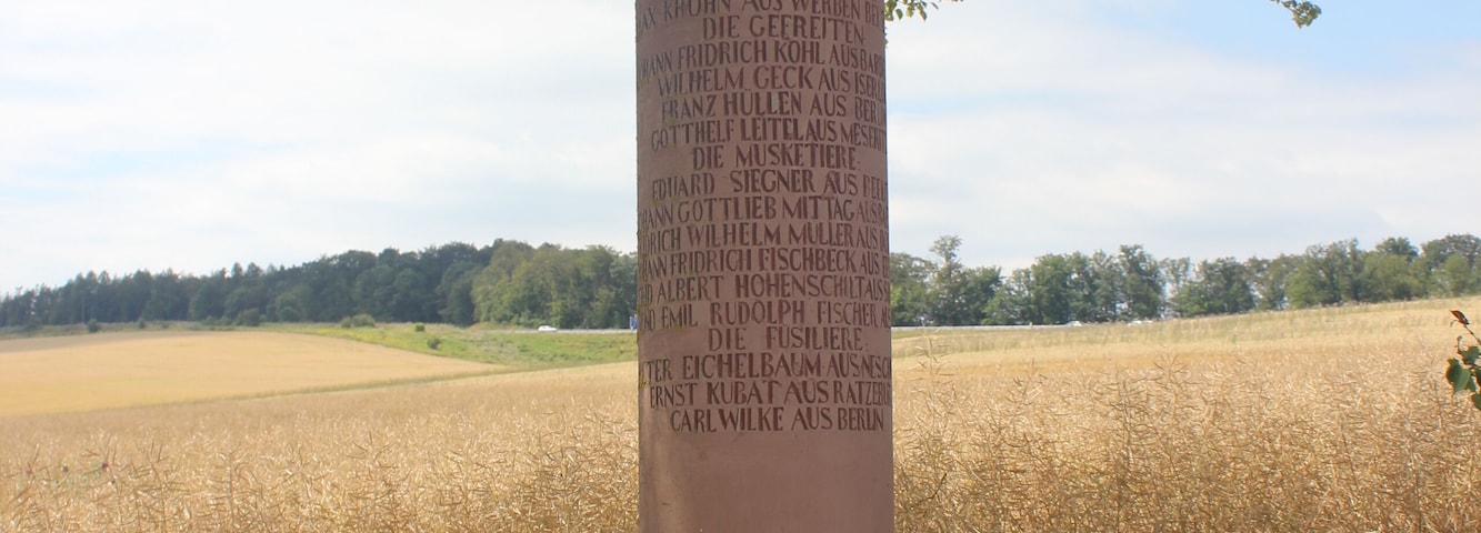 Denkmal für Gefallene des 3. Brandenburgischen Infanterie-Regiments No. 20 im Krieg von 1866. Runder Pfeiler mit achteckigem Sockel und Pickelhaube an der Spitze. Inschrift: DIE TAPFERN GEBLIEBENEN DES BRANDENBURGISCHEN INF. REGIMENTS No. 20. / 1866. / SECOND LIEUTNANT: / MAX KROHN AUS WERBEN BEI ZOSZEN. / DIE GEFREITEN: / JOHANN FRIDRICH KOHL AUS BARDEWITZ. / WILHELM GECK AUS ISERLOHN. / FRANZ HÜLLEN AUS BERLIN. / GOTTHELF LEITEL AUS MESERITZ. / DIE MUSKETIERE: / EDUARD SIEGNER AUS BEELITZ. / JOHANN GOTTLIEB MITTAG AUS BAERWALDE. / FRIDRICH WILHELM MÜLLER AUS DOBRILUCK. / JOHANN FRIDRICH FISCHBECK AUS EERCH. / GOTTFRID ALBERT HOHENSCHILT AUS SHLUNKENDORF. / EDMUND EMIL RUDOLPH FISCHER AUS BERLIN. / DIE FÜSILIERE: / PETER EICHELBAUM AUS NESCHHOLZ. / ERNST KUBAT AUS RATZEBUR. / CARL WILKE AUS BERLIN.