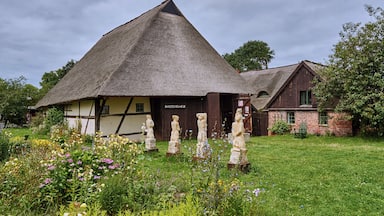 A thatched-roof house with a sign reading "RANSTECHEIMER" and stone sculptures in the garden.