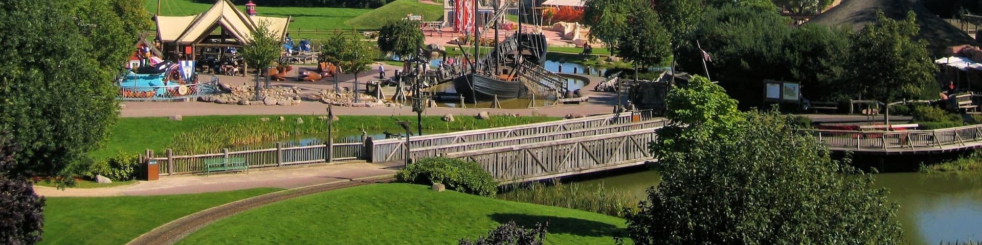 A theme park with a tall roller coaster, a water slide, and a bridge over a pond.