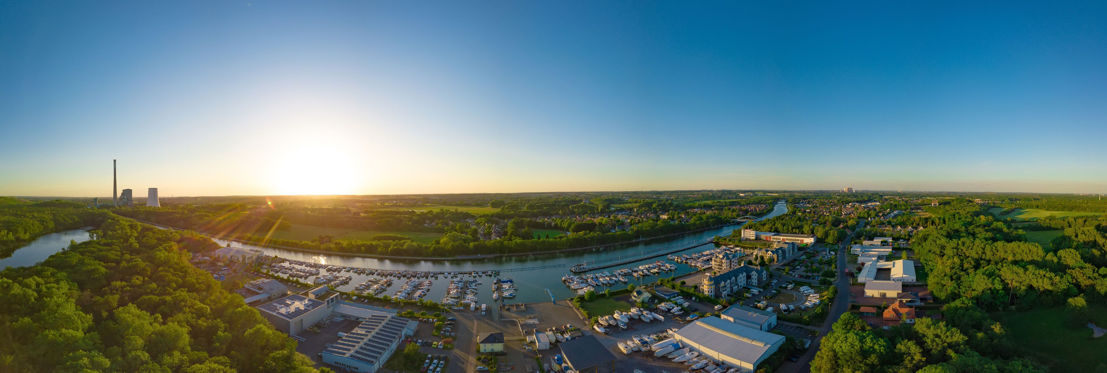 An aerial view of a marina with boats, a river, and surrounding greenery.