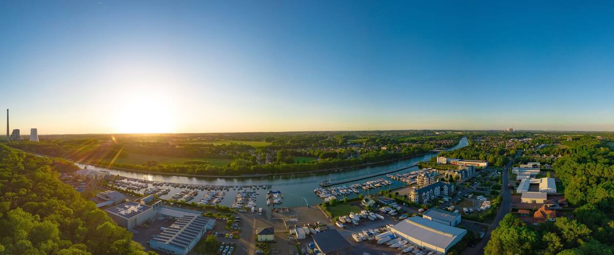 An aerial view of a marina with boats, a river, and surrounding greenery.