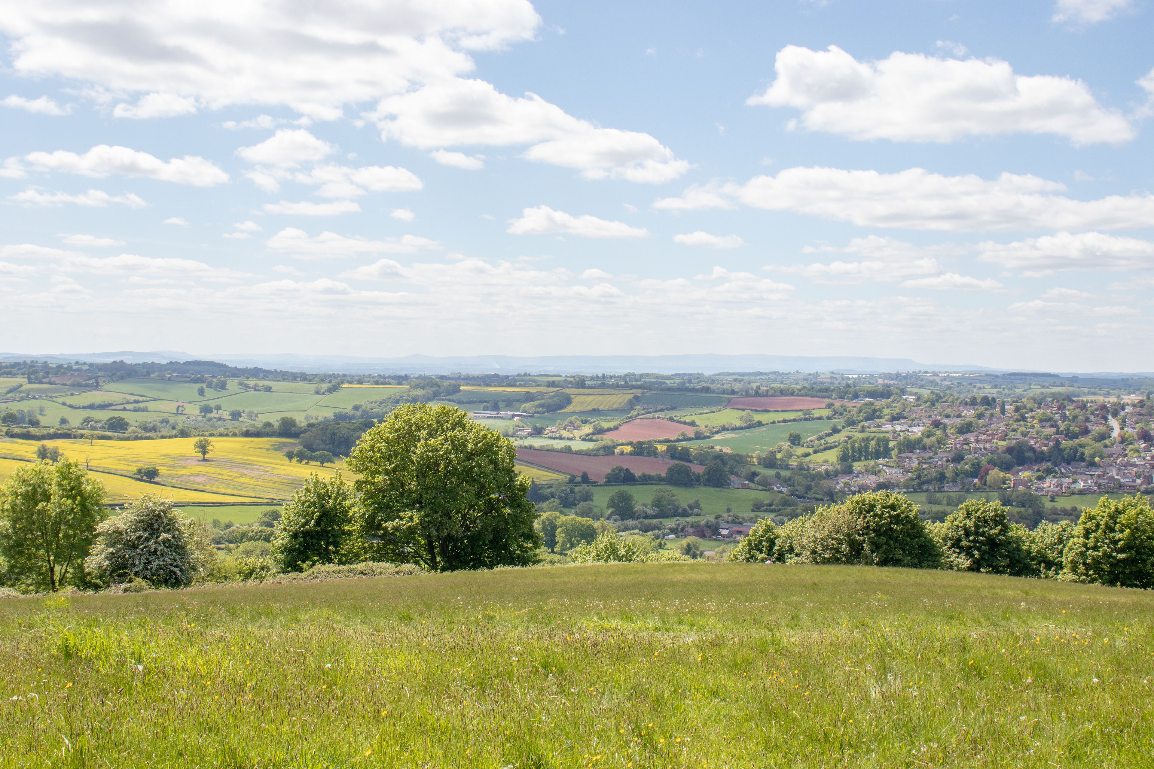 A rural landscape with rolling hills, fields, and a small village in the distance.