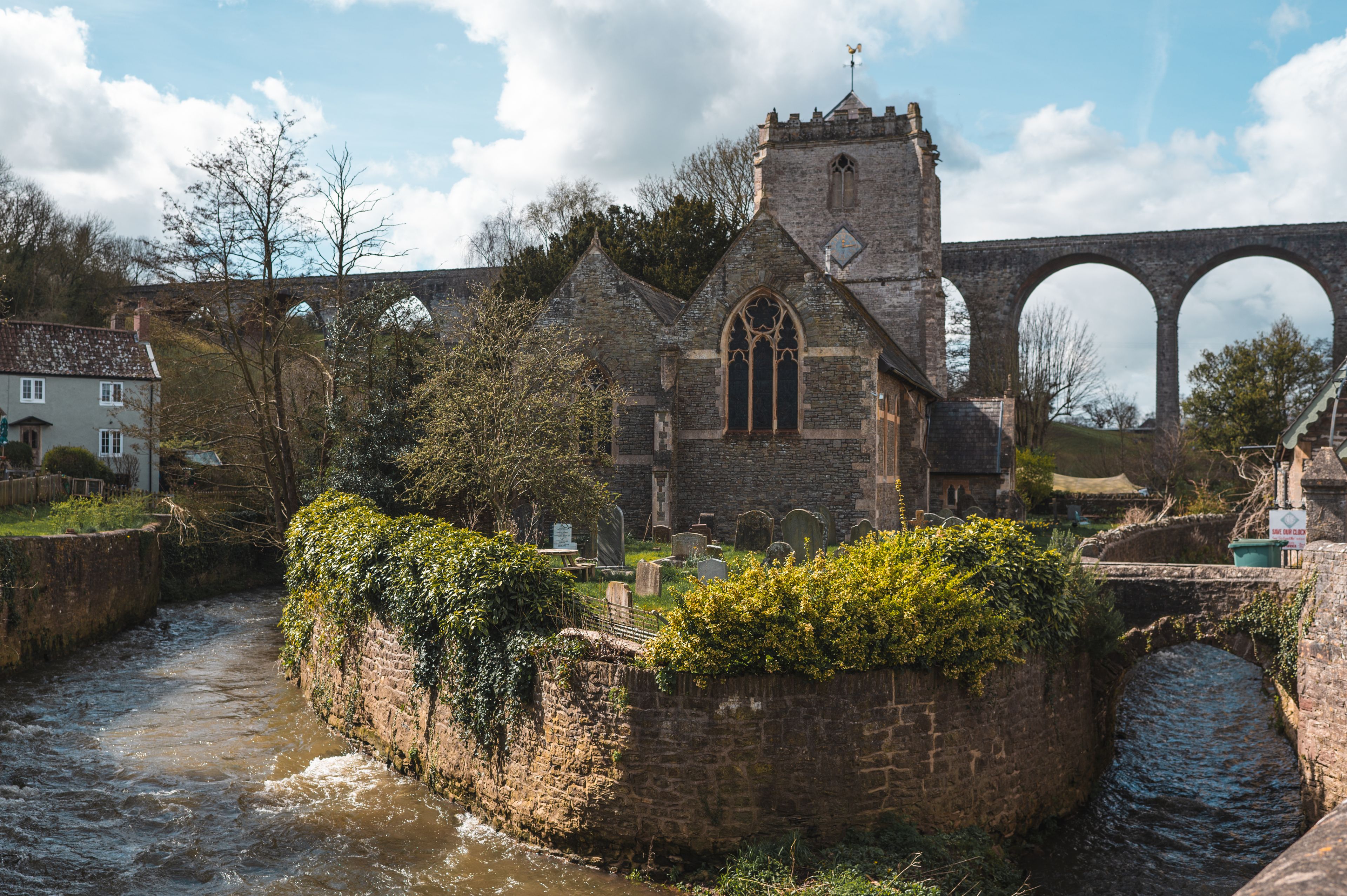 Eine historische Kirche mit einem Glockenturm, einer Steinbrücke und einem Fluss.