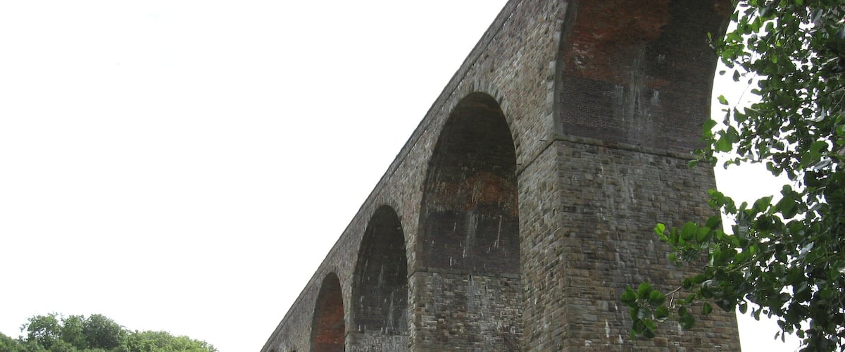 A large stone viaduct with multiple arches, surrounded by greenery and trees.