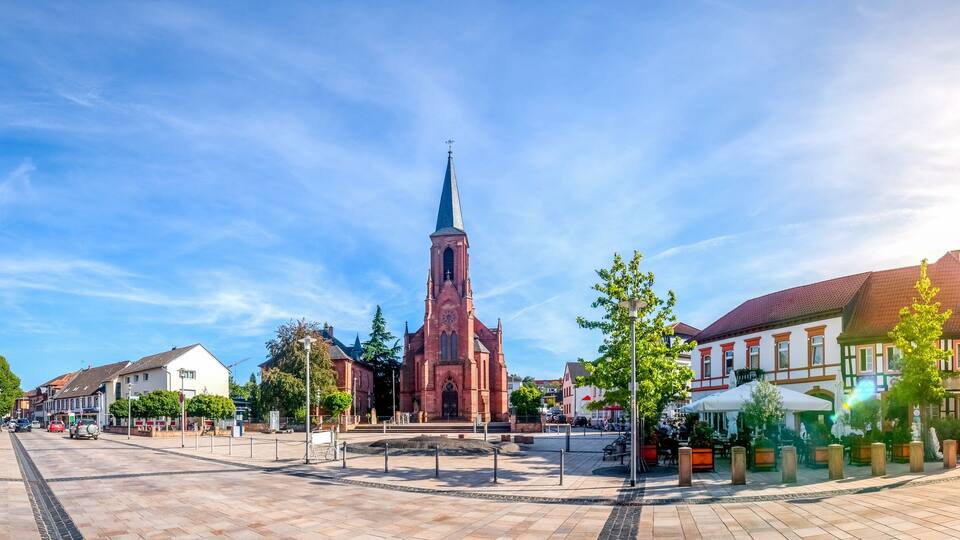 A town square with a prominent church steeple, historic buildings, and a central monument.