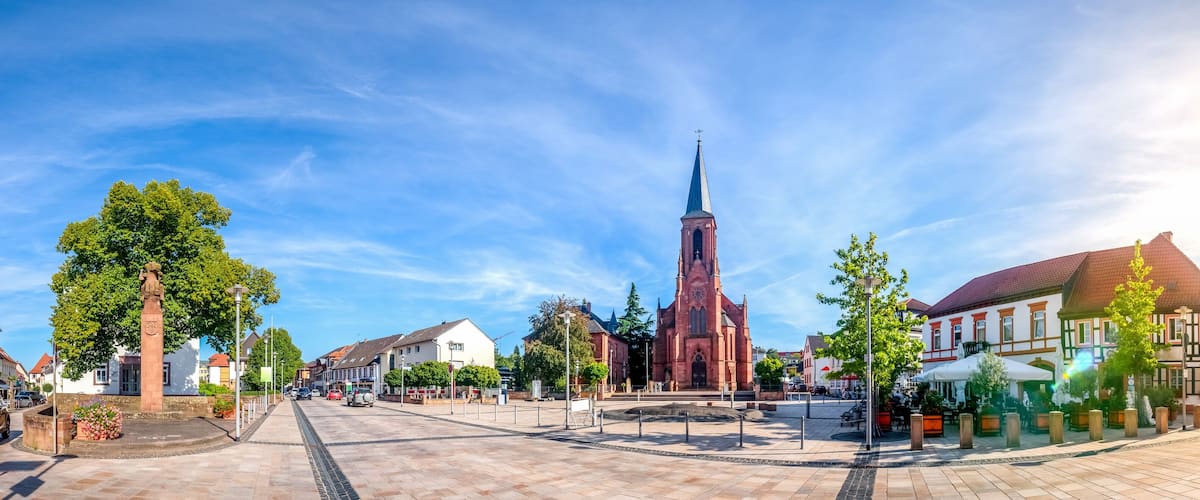 A town square with a prominent church steeple, historic buildings, and a central monument.