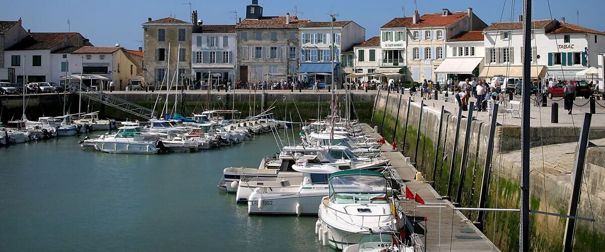 A marina with boats docked, a waterfront promenade, and buildings with signage.
