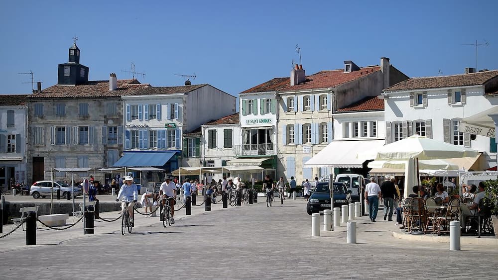 Une place animée, bordée de bâtiments historiques, de cafés, où l’on peut voir des gens se promener et faire du vélo.
