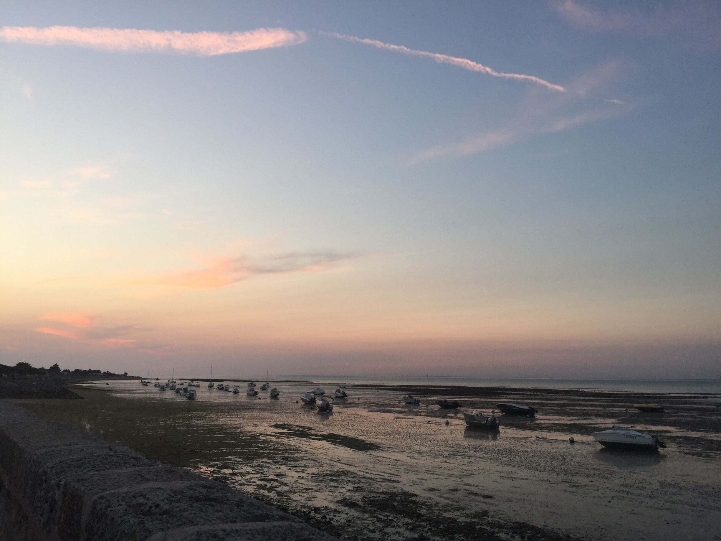 A beach at sunset with boats anchored in shallow water.