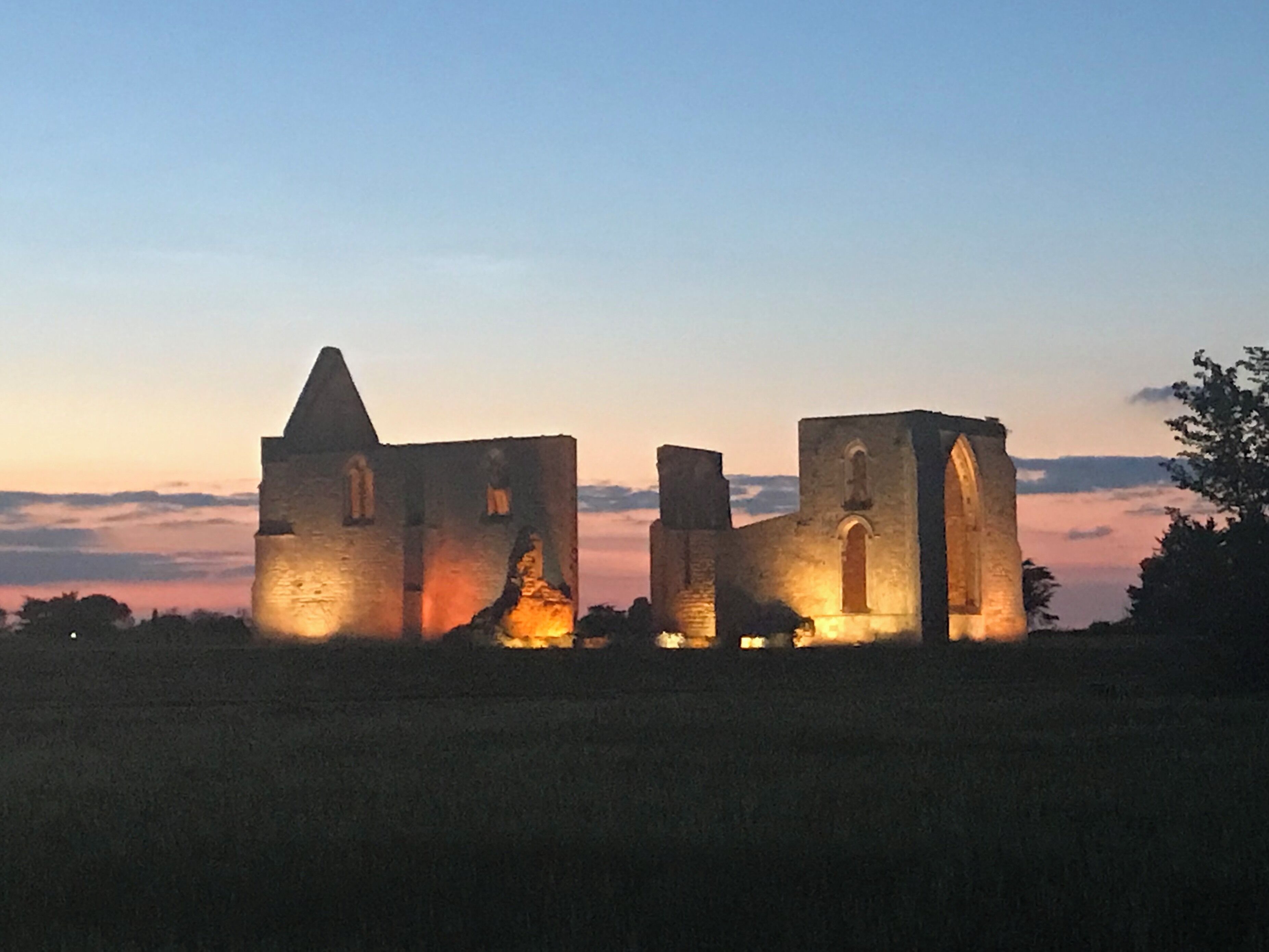 A medieval stone structure with arched windows and a pointed tower, illuminated by sunset.