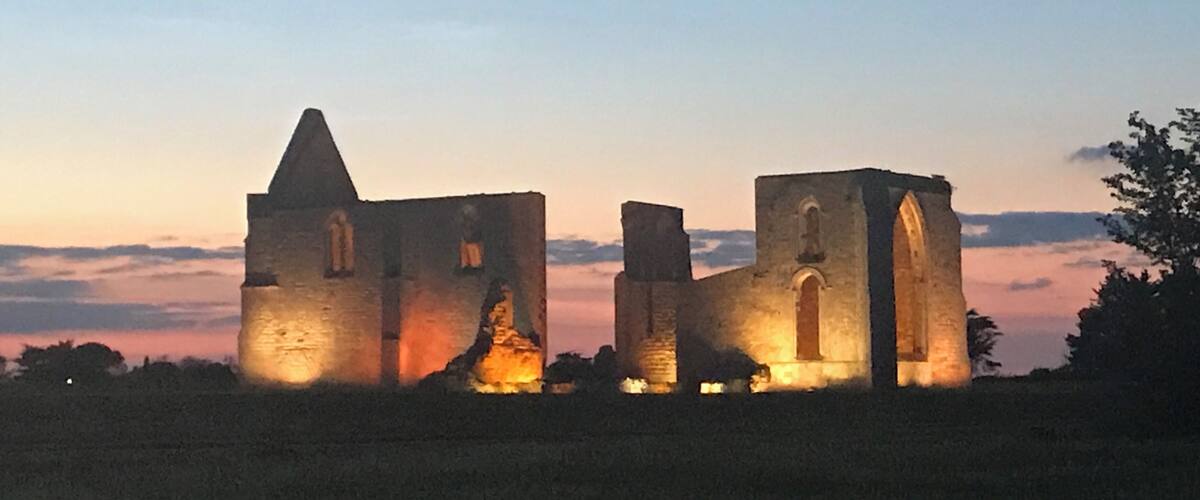 A medieval stone structure with arched windows and a pointed tower, illuminated by sunset.