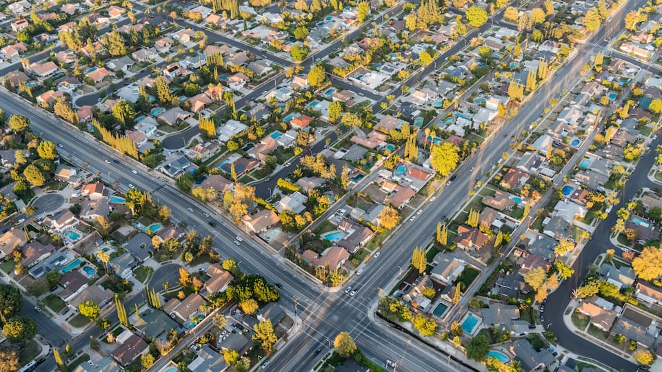 An aerial view of a residential area with houses, roads, and trees.